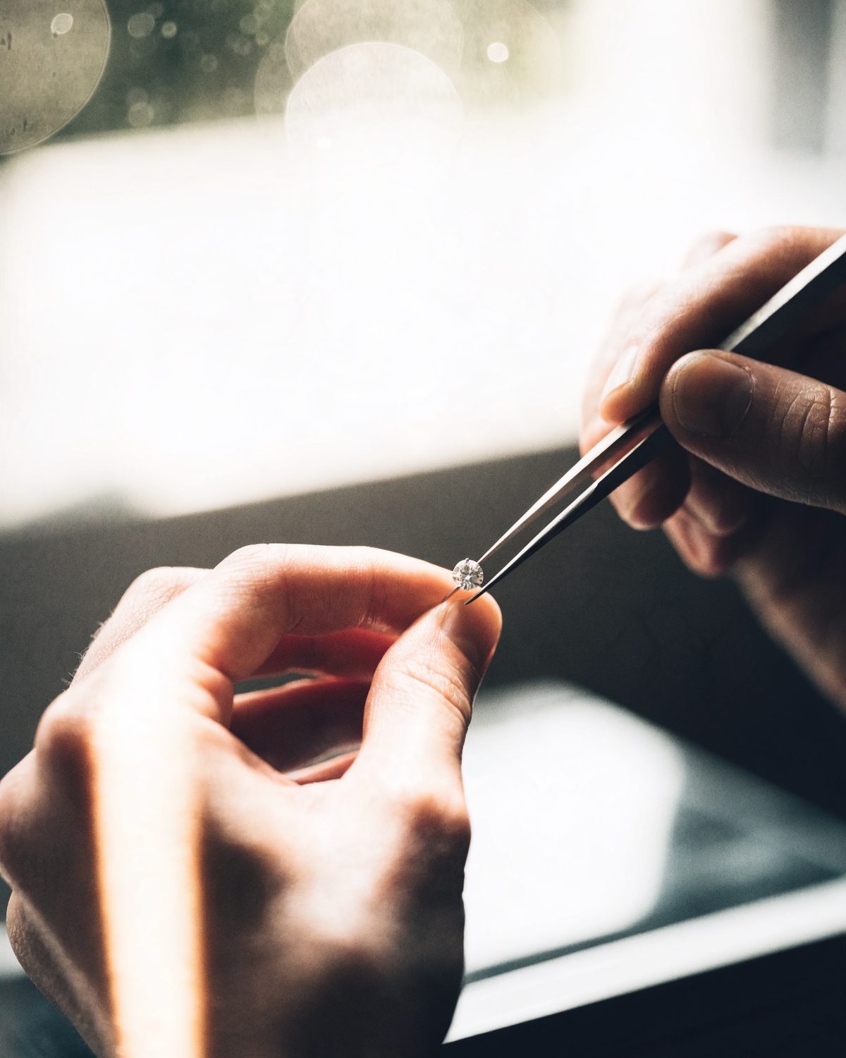 A jeweller holding a brilliant-cut diamond with tweezers at the bench